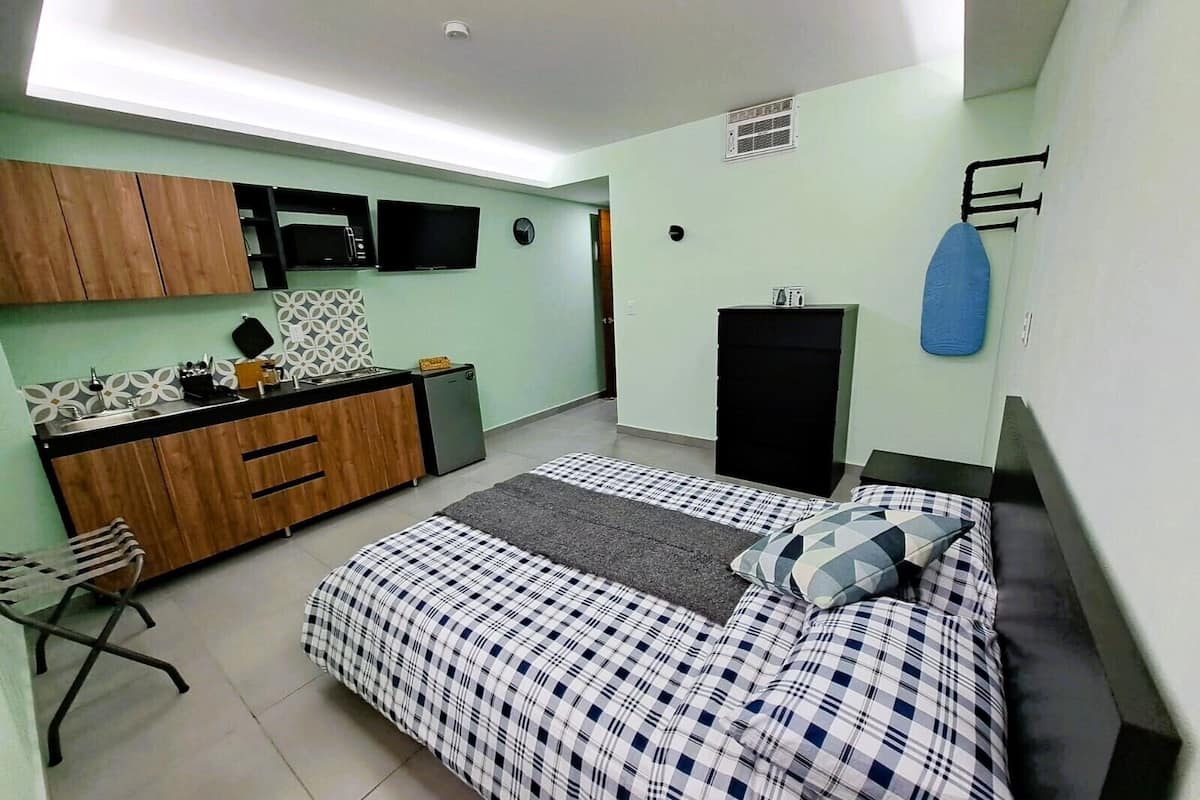 A compact bedroom with a bed, a small desk, a wardrobe, and a kitchenette.