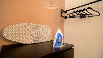 A neatly arranged ironing board with an iron, a hanging clothes rack, and a pillow with a chevron pattern on a dark wooden surface.