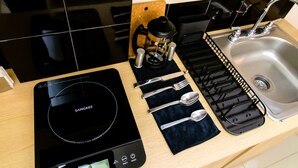 A kitchen with a black induction cooktop, a coffee maker, a sink, and a utensil holder.
