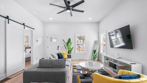 Ein modernes Wohnzimmer mit einer Couch, Sesseln, einem Couchtisch und einem an der Wand befestigten Fernseher.