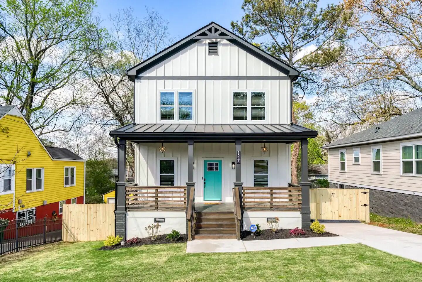 A two-story house with a front porch, a green door, and a small front yard.