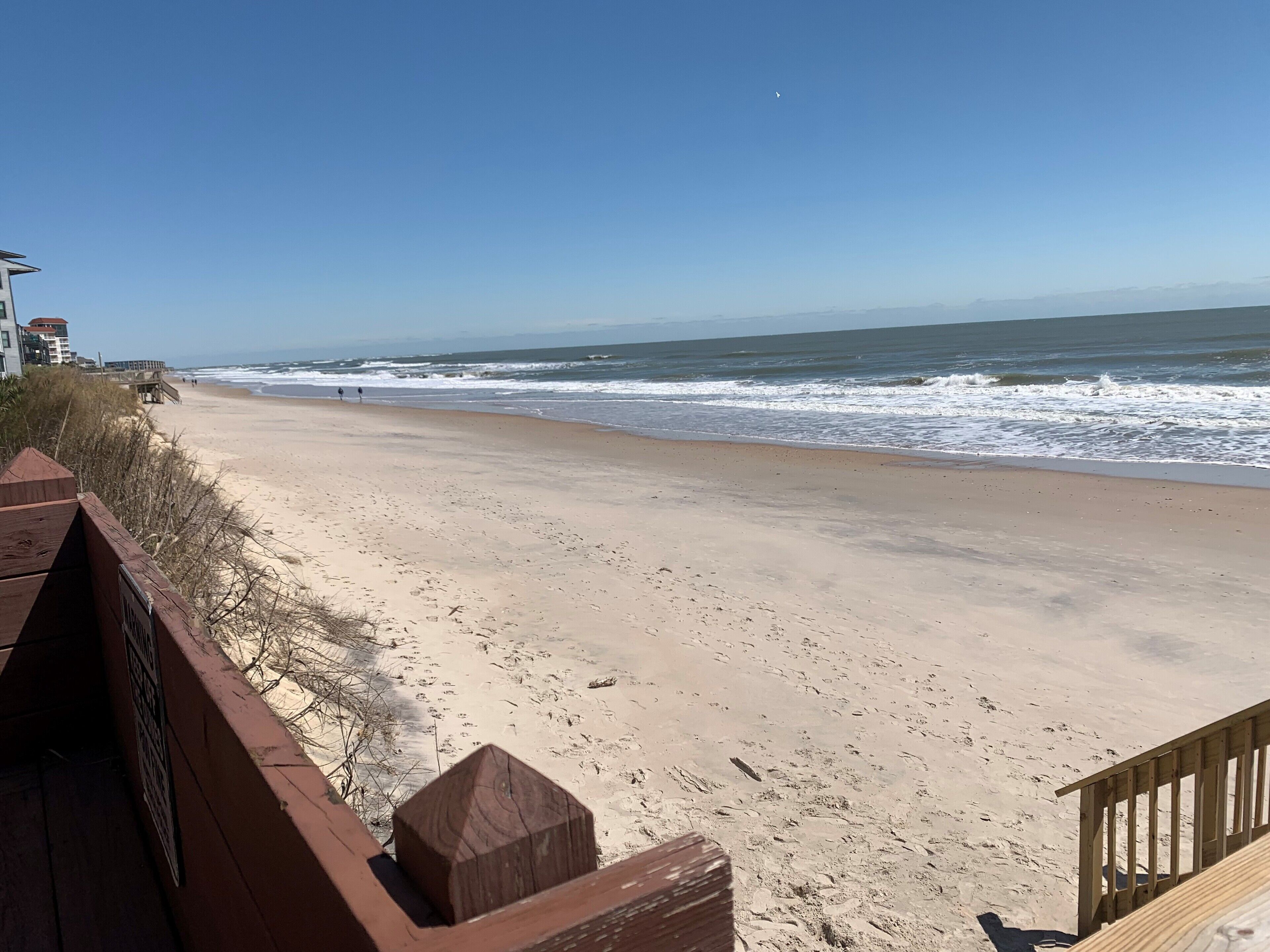 Een zandstrand met een houten looppad en een houten omheining.