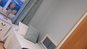 Ein Schlafzimmer mit Bett, Nachttisch, Lampe und einem Fenster mit Vorhängen.