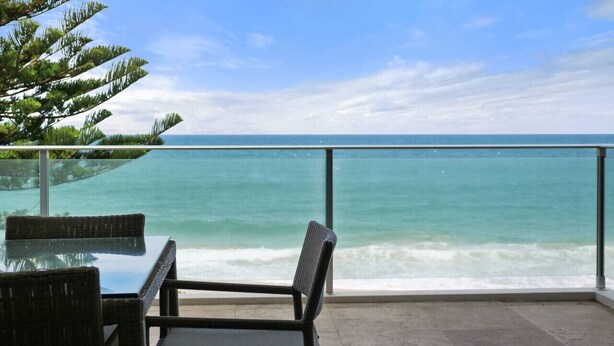 Un balcon avec une table et des chaises en verre donnant sur un océan turquoise.