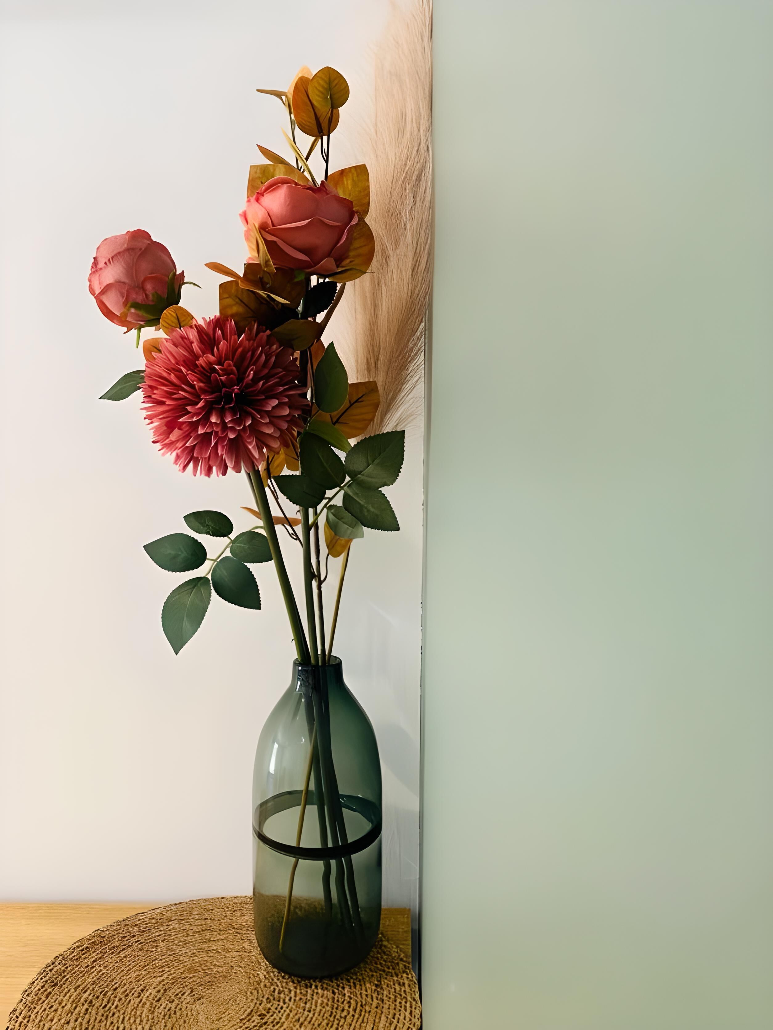 Een vaas met kunstbloemen en bladeren op een oppervlak met structuur.