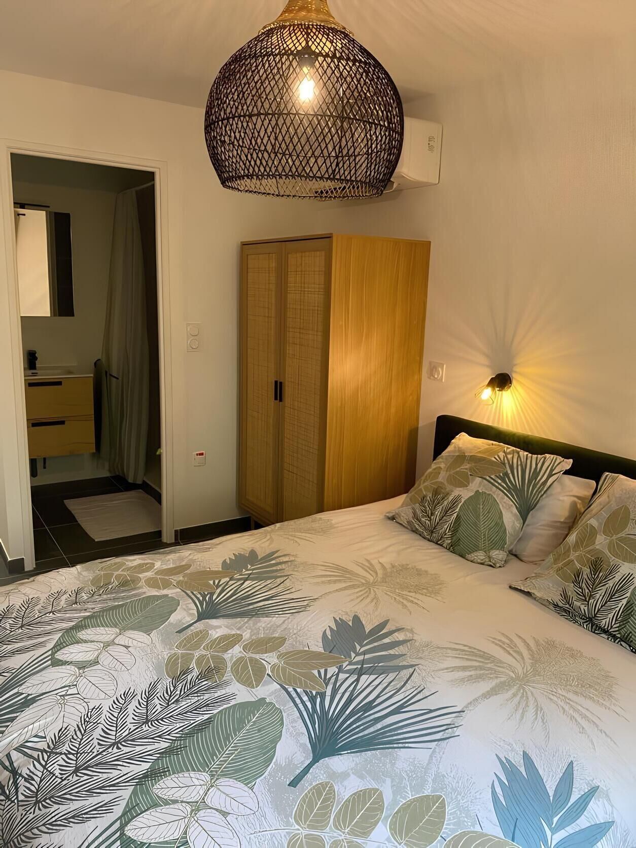 A bedroom with a bed, a wardrobe, a hanging light fixture, and a nightstand.