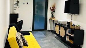 Un salón moderno con un sofá amarillo, un televisor de pantalla plana montado en la pared, una mesita con un jarrón y una puerta con paneles de vidrio esmerilado.