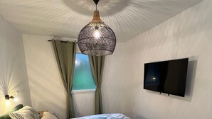 Un dormitorio con cama, televisor, ventana con cortinas y una lámpara de techo original.