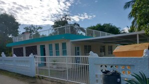 A two-story building with a white and teal exterior, a gated entrance, and a trash bin.