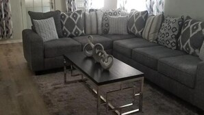 A living room with a sectional sofa, a coffee table, and patterned curtains.