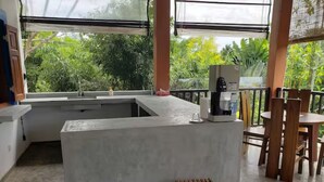 Une cuisine moderne avec un îlot central en béton, une machine à café et un petit tabouret en bois.