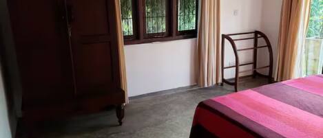 A bedroom with a bed, a wooden wardrobe, a window with curtains, and a small table.