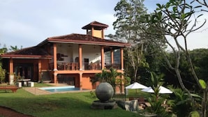 Une maison à deux étages avec une piscine, entourée d’un jardin bien entretenu et d’arbres.