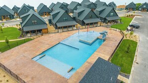 A resort with multiple chalet-style buildings, a central swimming pool, and a view of a lake.