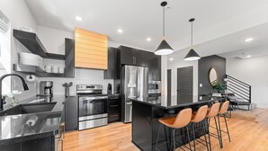 A modern kitchen with black cabinetry, stainless steel appliances, and a central island with bar stools.