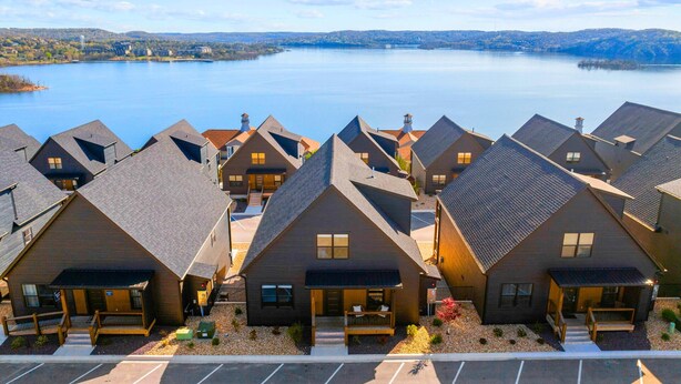 A cluster of modern, dark-colored cabins with sloped roofs, arranged in a row with a view of a large body of water and distant hills.