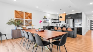 Una cocina moderna con armarios negros, electrodomésticos de acero inoxidable y una mesa de comedor de madera con sillas negras.