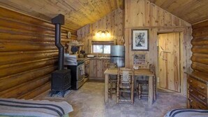 Hirsihirrestä rakennetun mökin sisätilat, joissa on keittiö, ruokailutila ja kaksi sänkyä.
