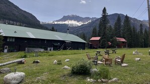 Eine rustikale Holzhütte mit einem grünen Dach, umgeben von einer Wiese mit Steinen und Holzbanken.