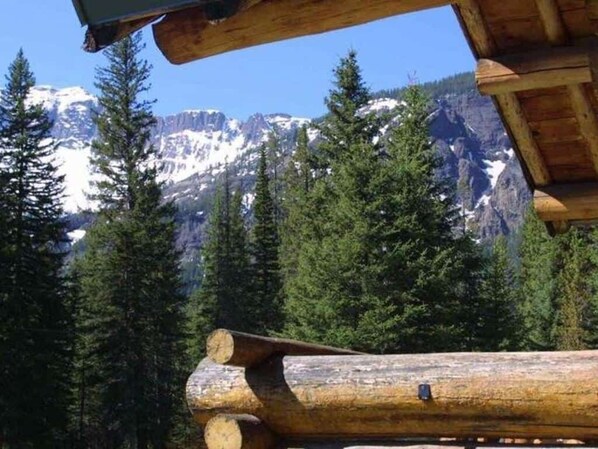 A log cabin with a view of snow-capped mountains and dense forest.
