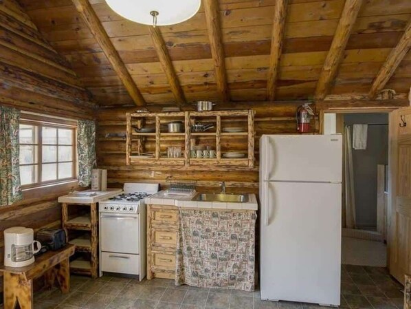 A rustic kitchen with wooden beams, a stove, a sink, and a refrigerator.