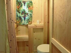 Une petite salle de bain en bois, équipée de toilettes, d’un lavabo et d’un espace douche.