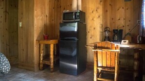 Eine kleine Küche mit Holzwänden, einem Edelstahlkühlschrank, einer Mikrowelle, einem Holztisch und einem Stuhl.