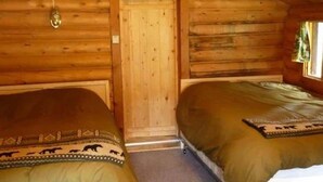 Eine Holzhütte mit zwei Betten, Holzwänden, einer Tür und einem kleinen Fenster.