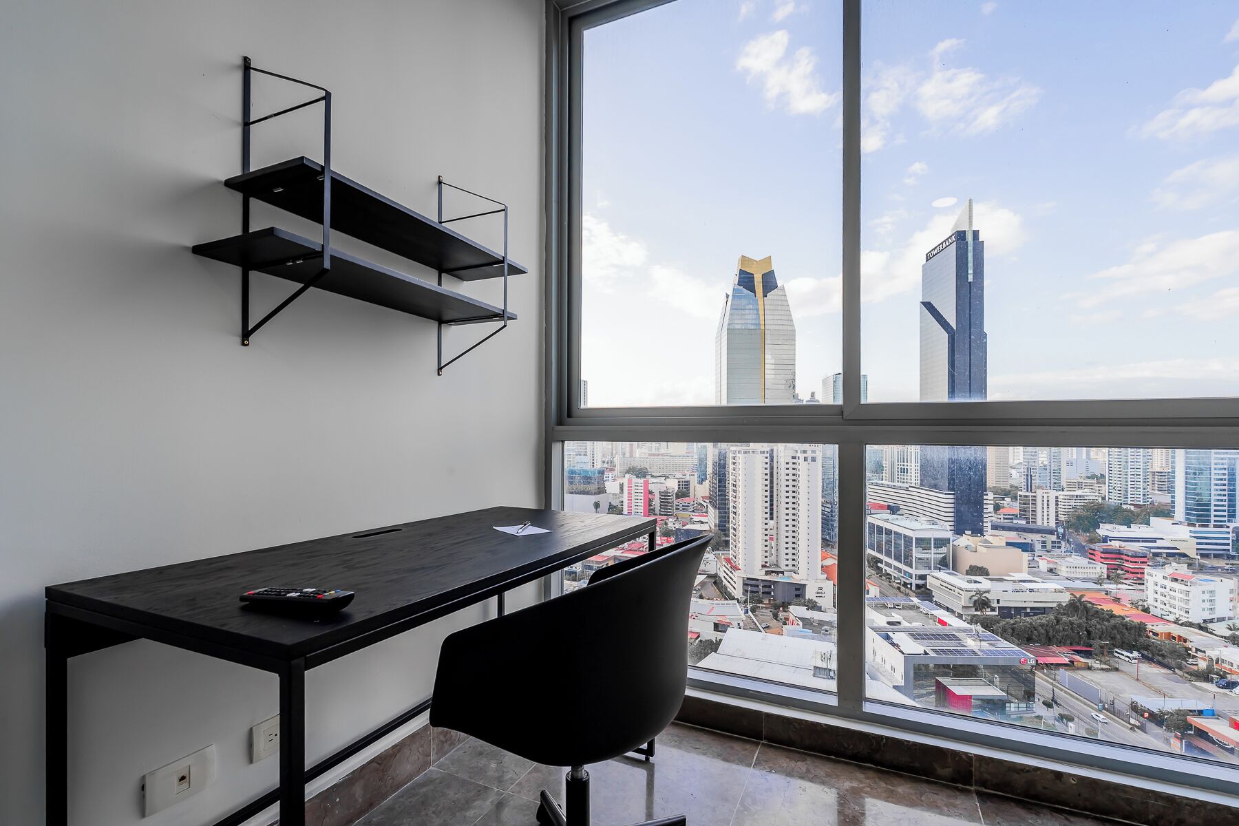 Un espacio de oficina moderno con escritorio, silla y estantería, con vista a un paisaje urbano de edificios altos.