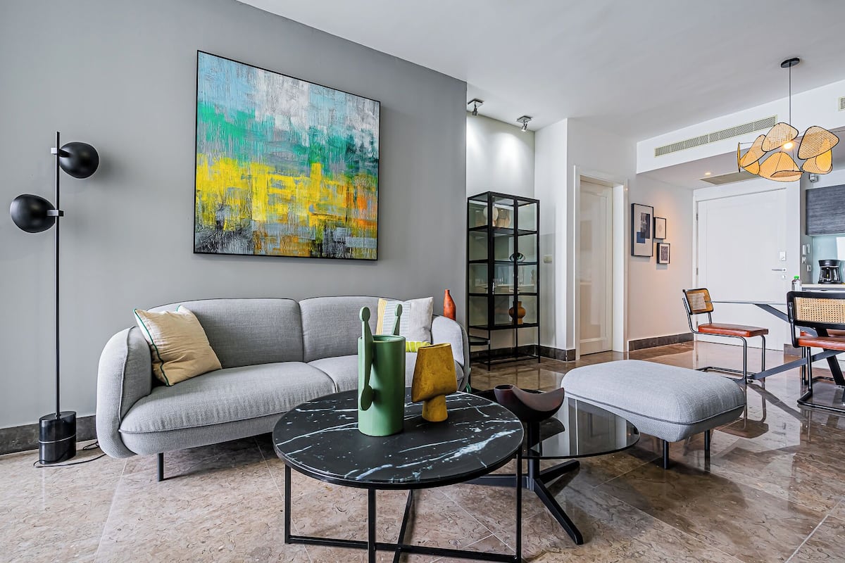 A modern living room with a grey sofa, a black coffee table, and a colorful abstract painting on the wall.