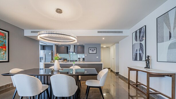 A modern dining area with a glass table, four chairs, a central light fixture, and a kitchen in the background. - Yoo by Wynwood House (Panama City)