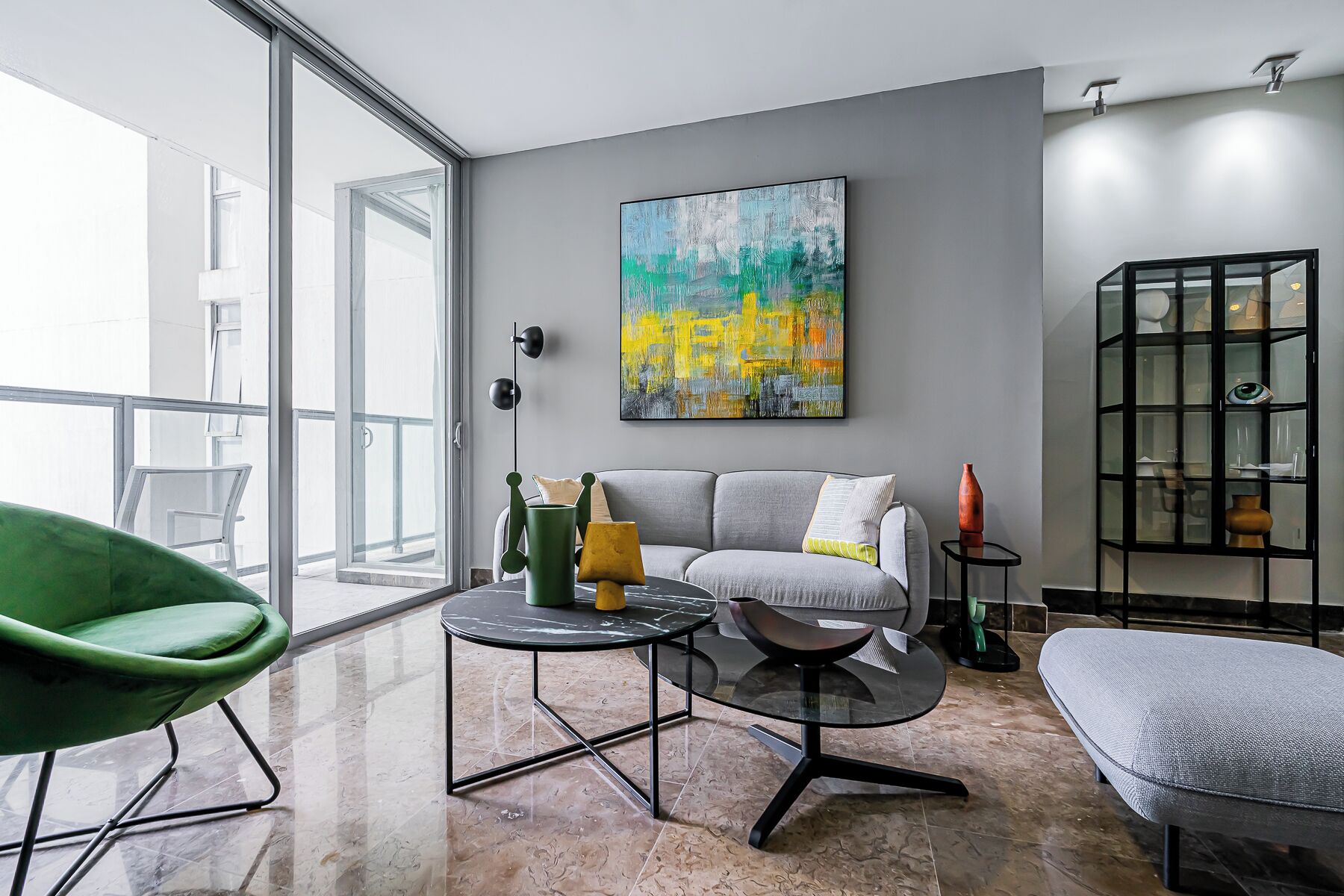 A modern living room with a gray sofa, a green chair, a glass coffee table, and a large abstract painting on the wall.
