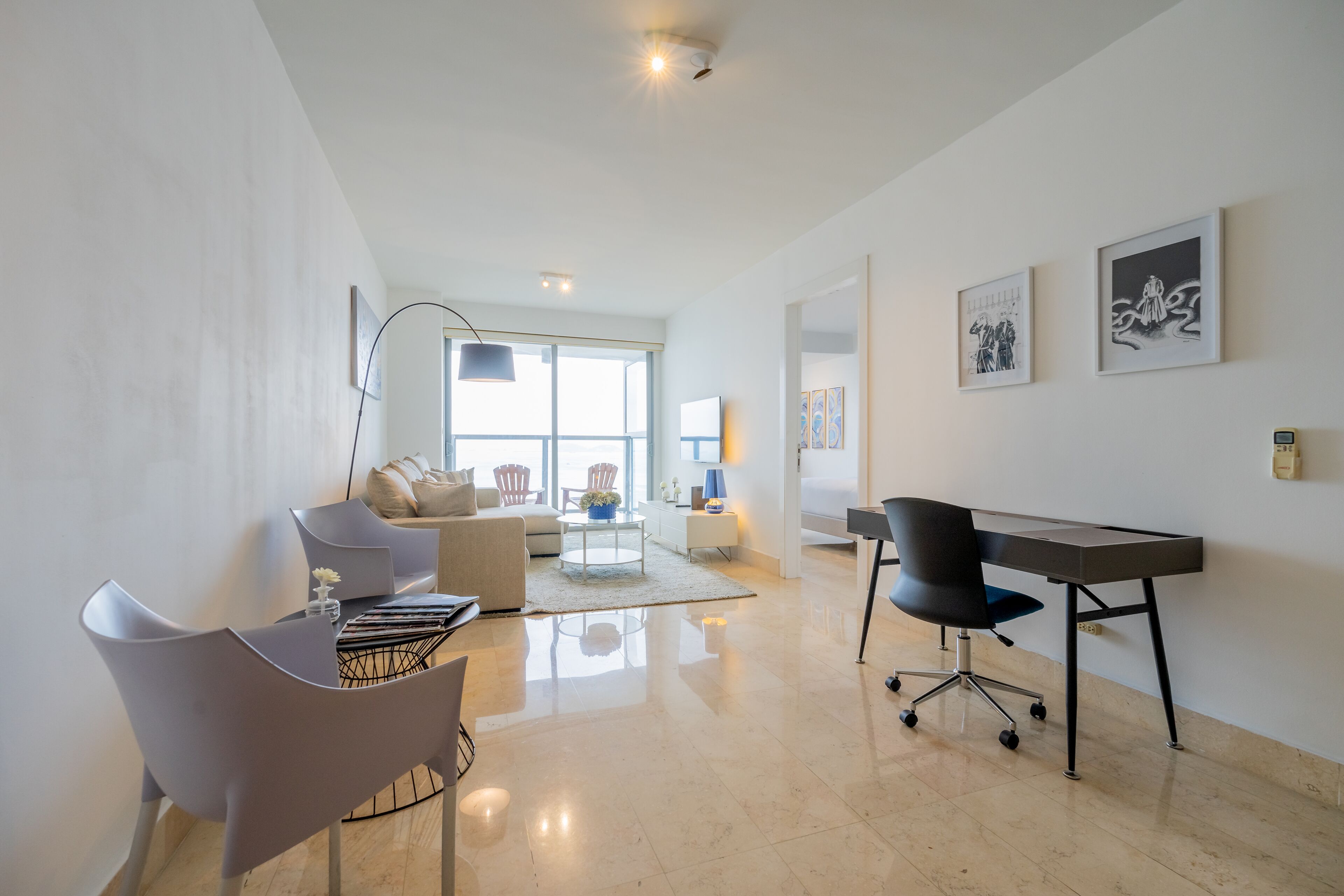 A modern living room with a sofa, a dining table, and a desk. There are two framed pictures on the wall.