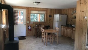 A wooden-paneled kitchen with a dining table, chairs, a refrigerator, and a stove. - Comfy cabin is situated on the Silver Gate property which overlooks 10,000ft tall mountain peaks surrounding the town. (SILVER GATE)