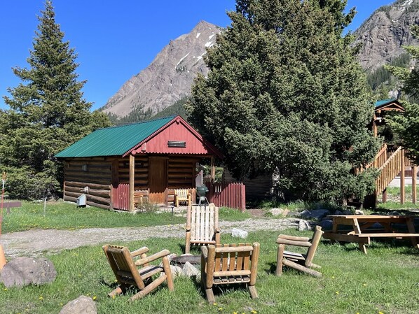 A rustic log cabin with a green roof, surrounded by a grassy area with wooden benches.