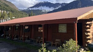 A rustic log cabin motel with a red roof, numbered rooms, and a view of snow-capped mountains.
