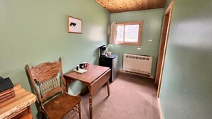 Una habitación pequeña y acogedora con techo de madera, una mesa con sillas, un radiador y una ventana con cortinas.