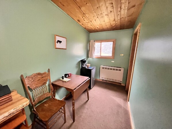 Une petite pièce agréable, avec un plafond en bois, une table entourée de chaises, un radiateur et une fenêtre avec des rideaux.