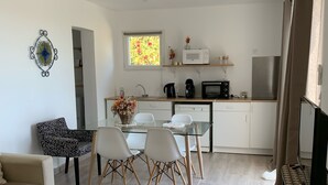 A modern kitchen with white cabinets, a microwave, and a refrigerator. There is a dining area with a glass table and chairs, and a sofa. - Charmant T2 vue mer (Bastia)