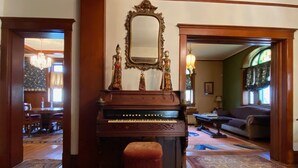 A grand piano in a spacious living room with a large mirror above it, wooden floors, and a cozy seating area with a sofa and armchairs. - Historic home in the heart of Poplar Bluff (Poplar Bluff)