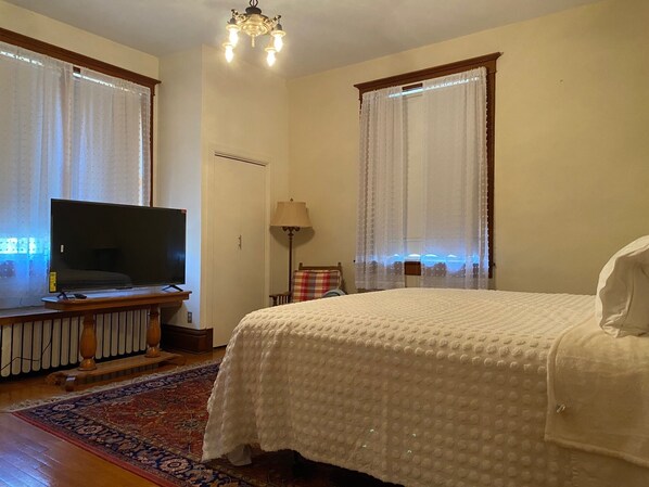 Camera d'albergo con un letto grande, una televisione su un supporto in legno, una lampada e una finestra con tende.