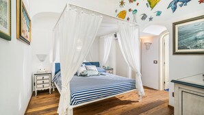 Ein Schlafzimmer mit Himmelbett, gestreifter Bettwäsche, einem Nachttisch und einer Wand mit Wandbildern von Fischen und Seesternen.