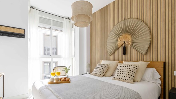 Un dormitorio moderno con una cama grande, un panel de pared de madera, un ventilador colgante y una bandeja de desayuno en la mesita de noche.