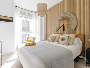 A modern bedroom with a large bed, a wooden panel wall, a hanging fan, and a breakfast tray on the nightstand. - Evergreen Centre Apartment Living4malaga (Málaga)