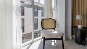 Un apartamento moderno con un ventanal grande, una silla de mimbre, una mesita auxiliar con una lámpara y un panel de pared de madera.