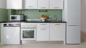 Una cocina moderna con armarios blancos, microondas, lavaplatos, fregadero y refrigerador.