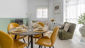 Un comedor con una mesa redonda dispuesta para cuatro personas, rodeada de sillas amarillas. Un candelabro moderno cuelga sobre la mesa.