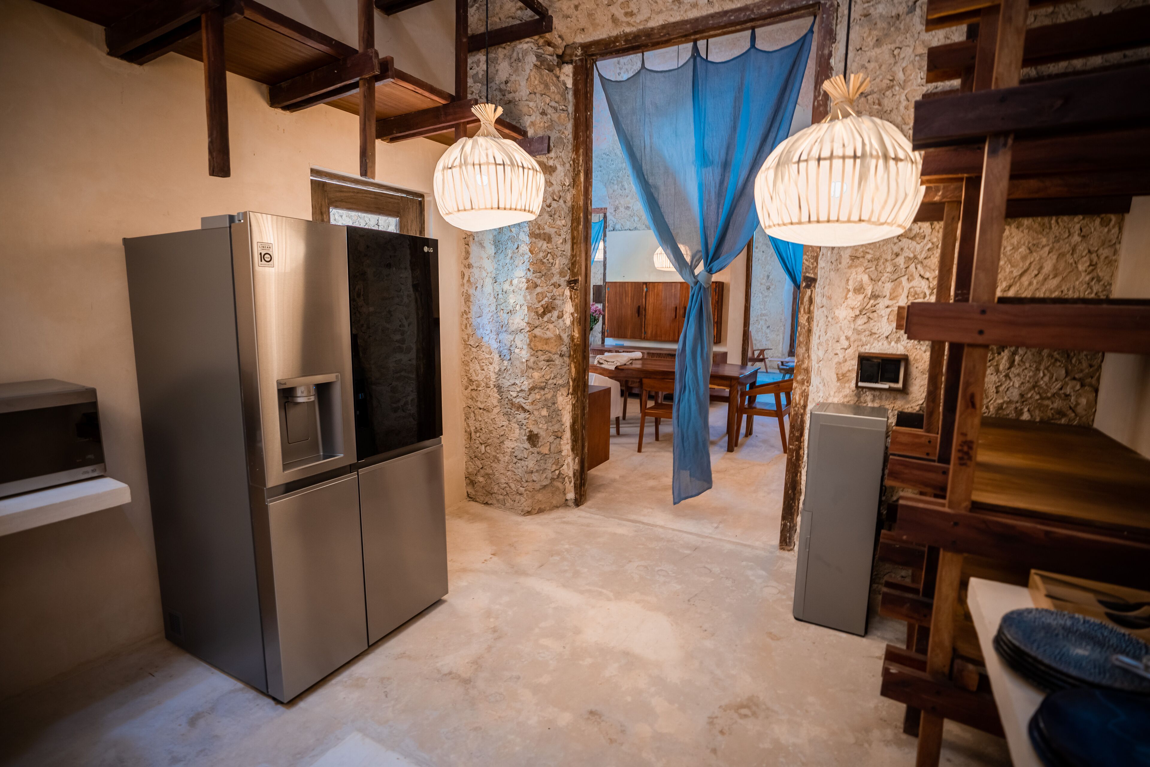 Una cocina con refrigerador de acero inoxidable, vigas de madera, paredes de piedra y una cortina azul.