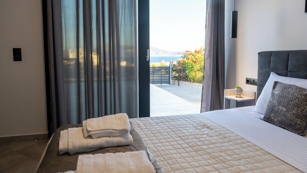 A modern bedroom with a large bed, a view of the outdoors, and a small bedside table with a lamp.