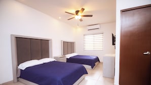 Una camera d'albergo con due letti, un ventilatore a soffitto, un condizionatore d'aria e una porta.